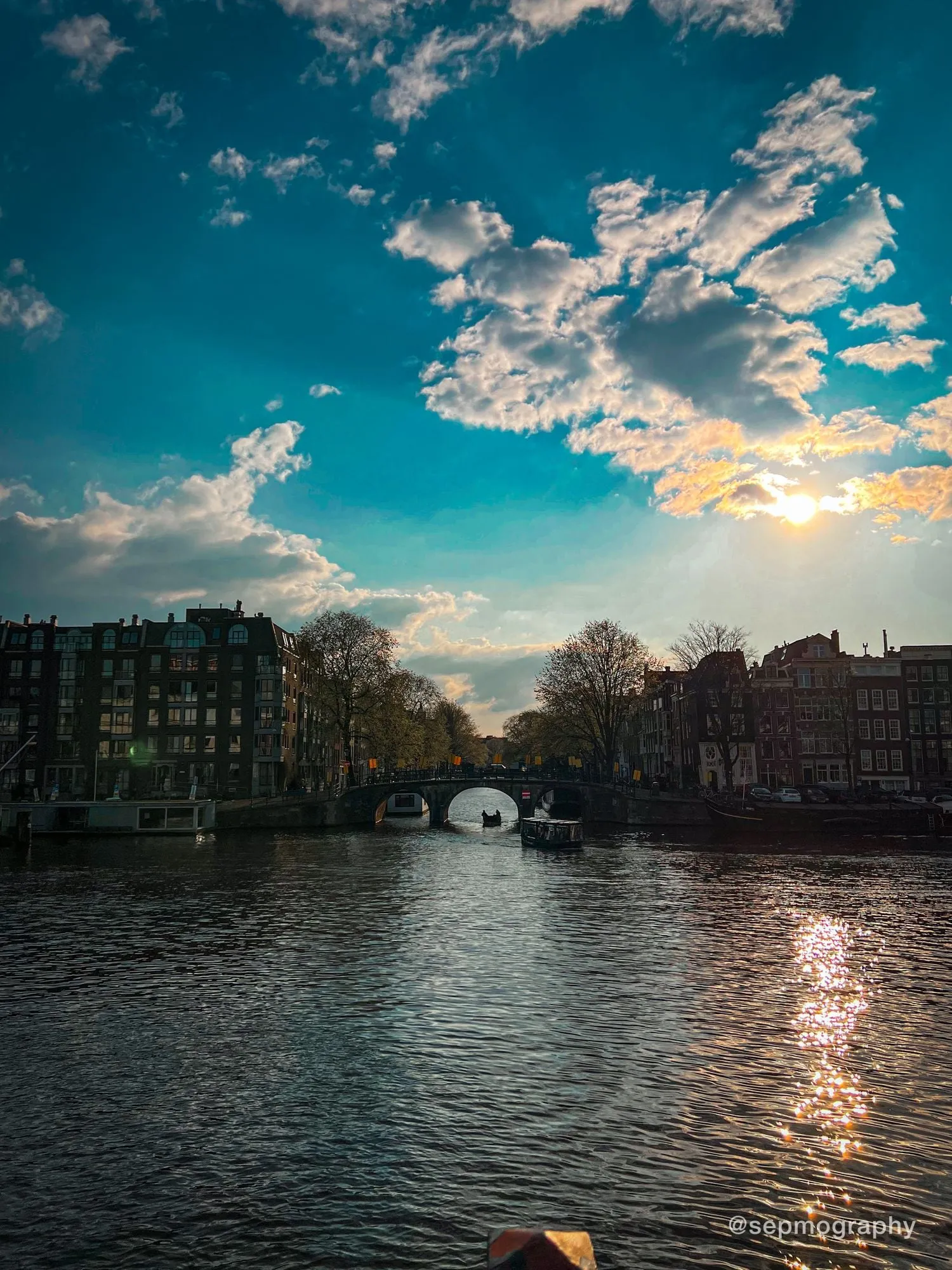 A canal at low sun, an arched bridge in the distance and light scattered across the water
