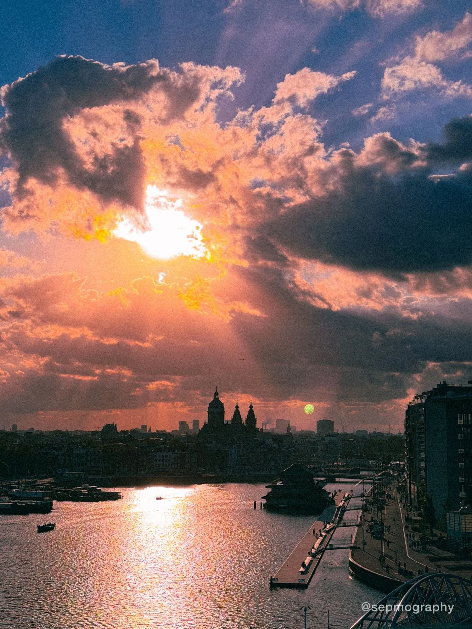 Sun breaking through heavy cloud over the IJ, with the domes of the Basilica of Saint Nicholas in silhouette