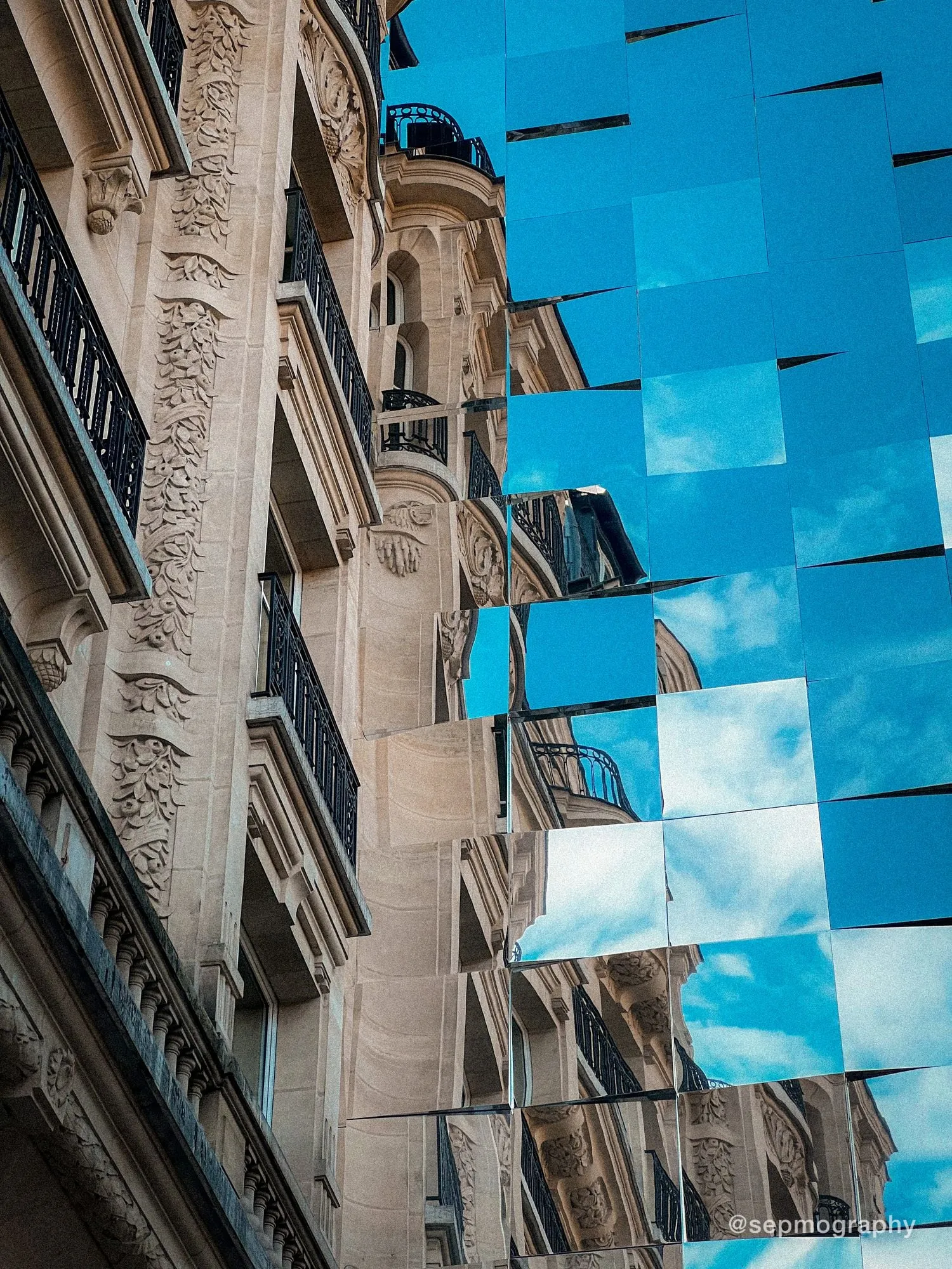 A carved stone facade beside a wall of mirrored panels reflecting it back in fragments